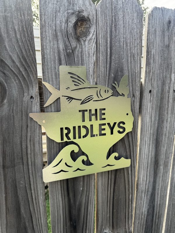 Photo of a laser-cut metal sign reading The Ridleys, hung on a wooden fence